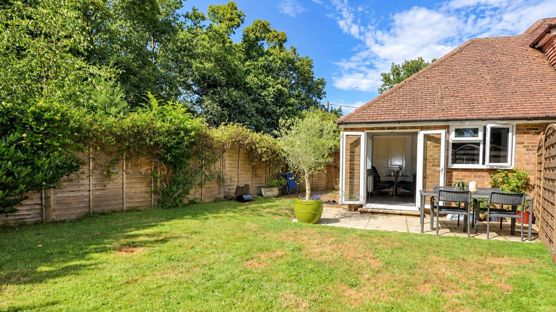 A backyard with a patio, a small garden, and a brick house.