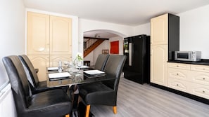 Una cocina moderna con comedor, que incluye un refrigerador negro, un microondas y una mesa de comedor de vidrio con sillas negras.
