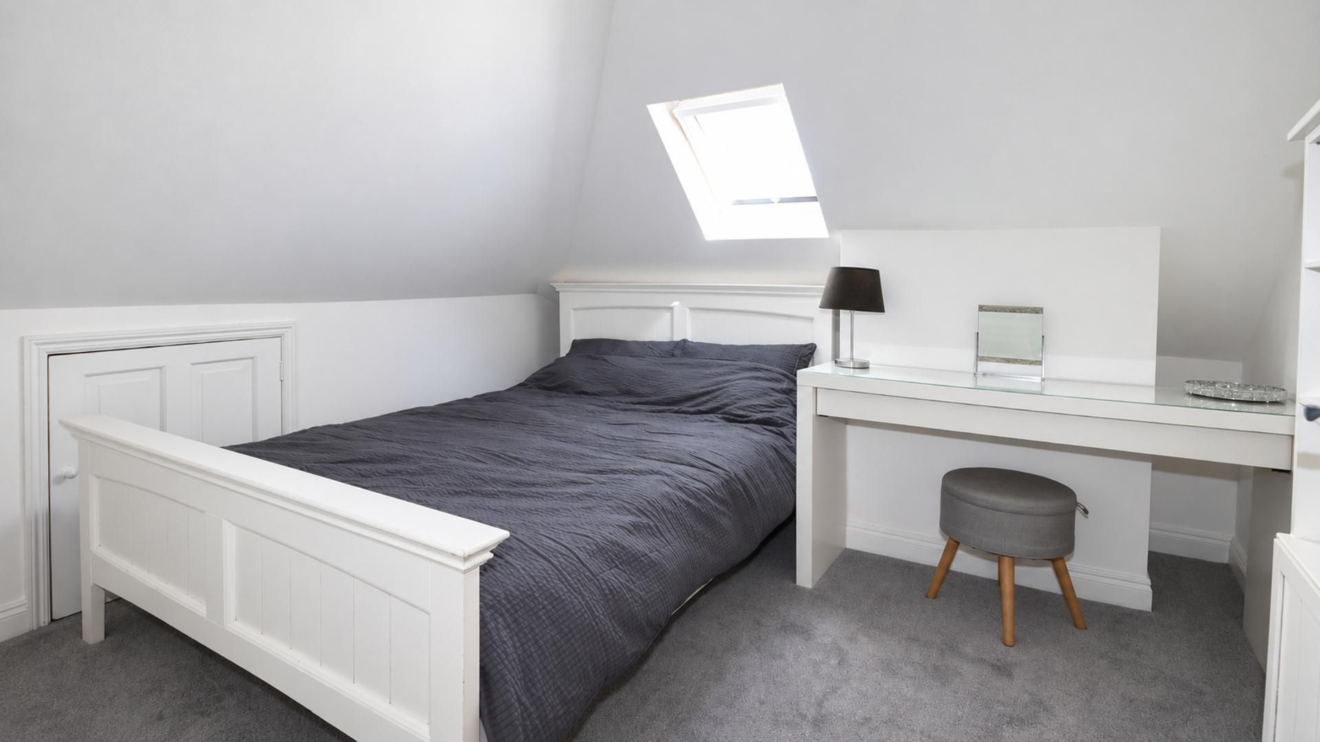 A bedroom with a bed, a desk, a chair, a lamp, and a window.