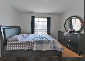Ein Schlafzimmer mit einem Bett, einem Schminktisch, einem Spiegel und einem Fenster mit Vorhängen.