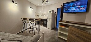 A compact living space with a kitchenette, a dining area with bar stools, a flat-screen TV mounted on the wall, and a wooden cabinet. - Hotel Cheval Blanc (Villa Gesell)