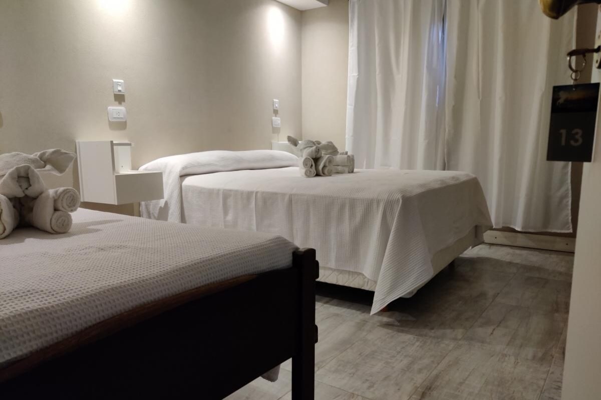 A hotel room with two beds, a wooden chair, a bedside table, and a curtain.