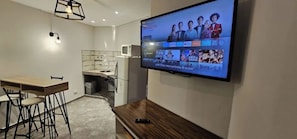 A modern living room with a flat-screen TV mounted on the wall, a wooden dining table with chairs, and a kitchen area with a microwave and cabinets. - Hotel Cheval Blanc (Villa Gesell)