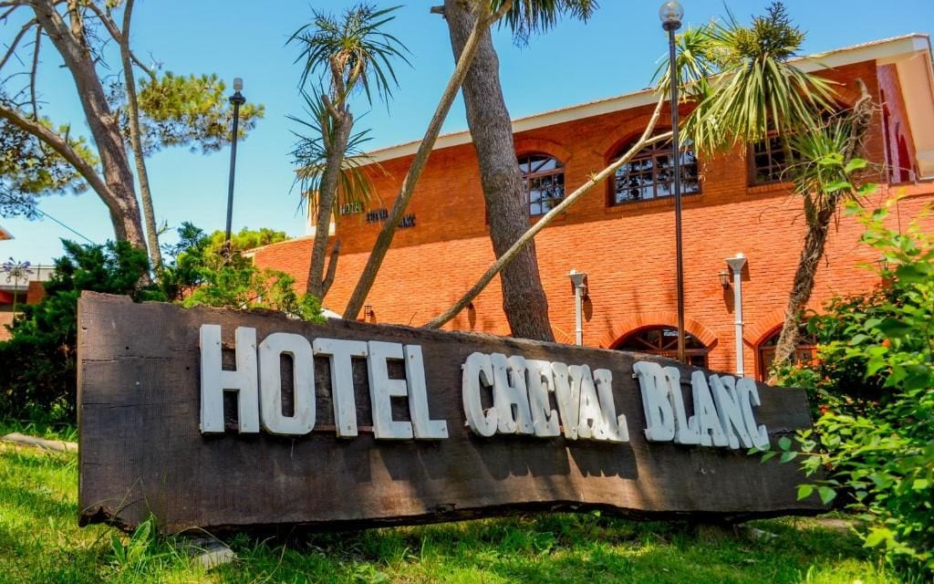 Un letrero de madera con el texto 'HOTEL CHEVAL BLANC' frente a un edificio con paredes de ladrillo rojo y ventanas de arco.