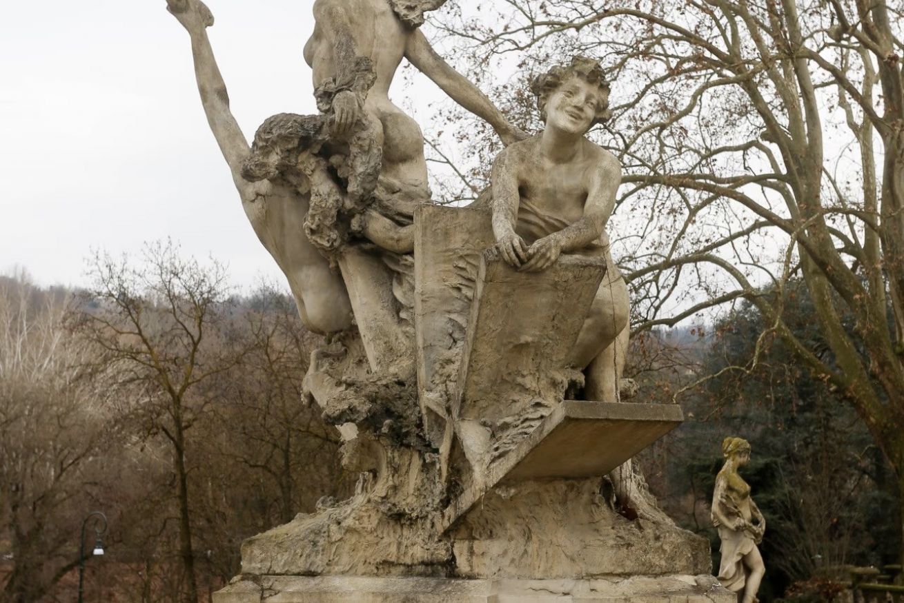 A stone sculpture of a seated figure with a child, surrounded by trees.