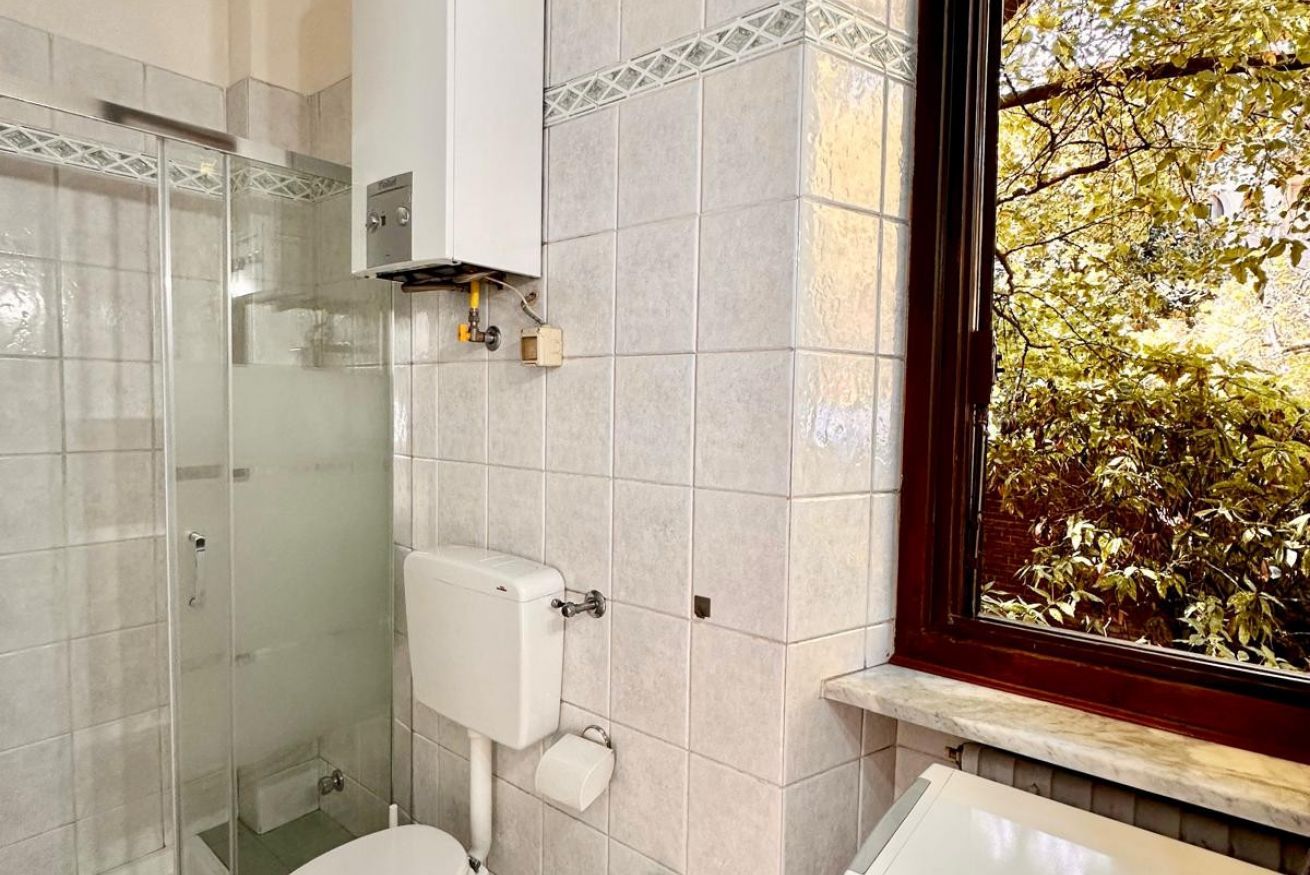 Une salle de bain équipée de toilettes, d’une douche à parois de verre et d’une fenêtre donnant sur la verdure.