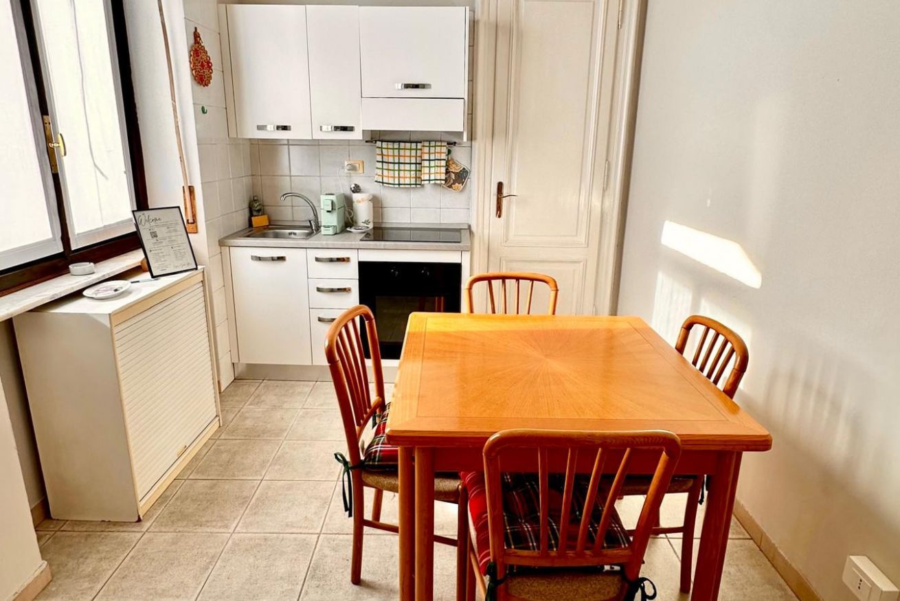 Une cuisine compacte avec des meubles blancs, un petit plan de travail et une table à manger avec quatre chaises.
