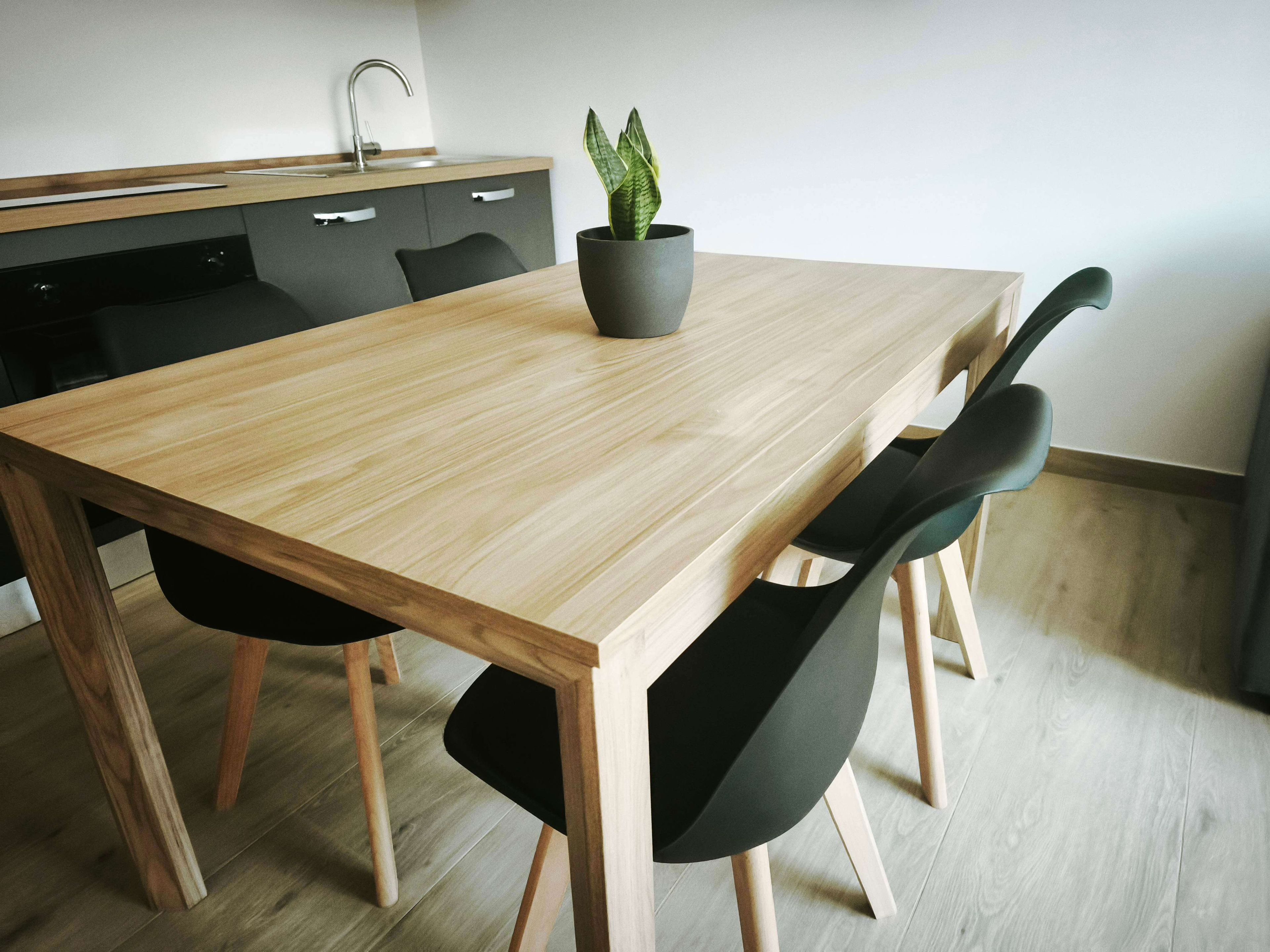 Une cuisine moderne avec une table en bois, des chaises noires, une plante en pot et un évier encastré.