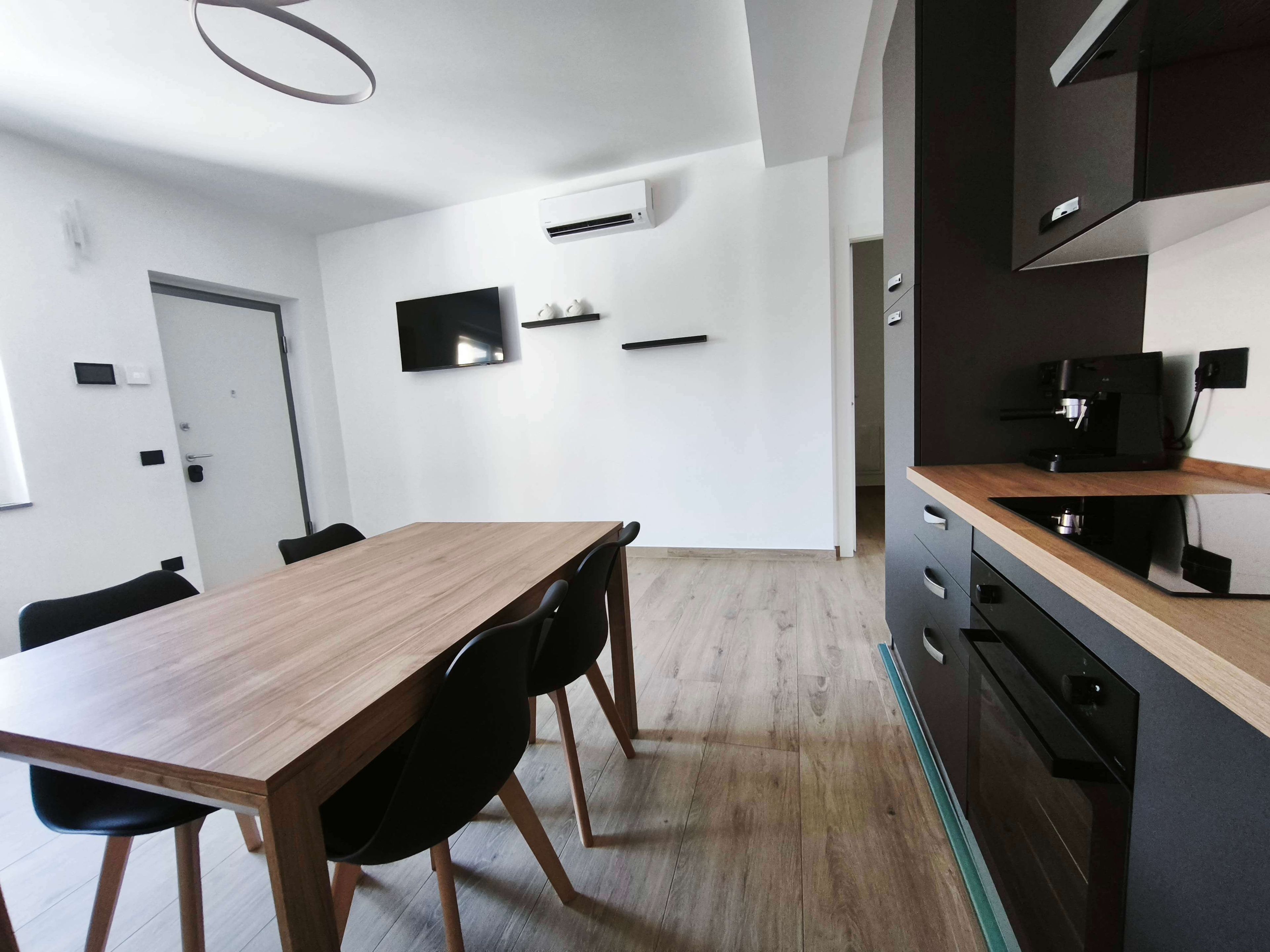 A modern kitchen with a built-in oven, a coffee machine, and a flat-screen TV mounted on the wall.