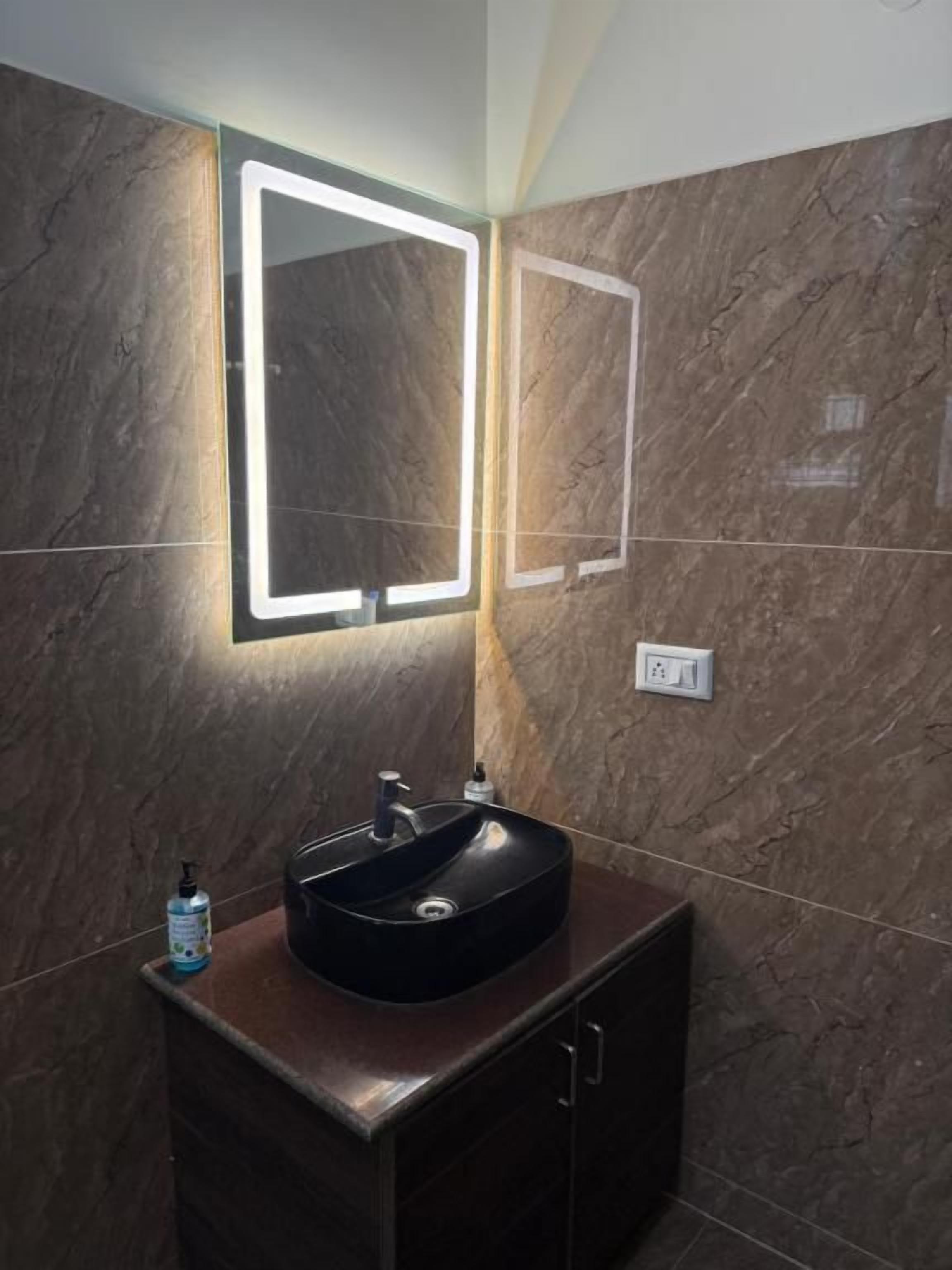 Un baño con un lavamanos negro, un espejo con bordes iluminados y una pared de mármol.