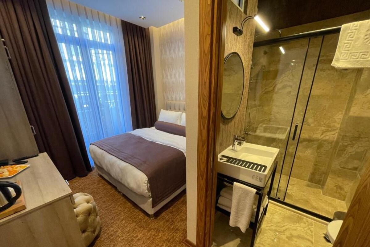 Ein Hotelzimmer mit Bett, Schreibtisch, Badezimmer mit Dusche und einem großen Fenster mit Vorhängen.