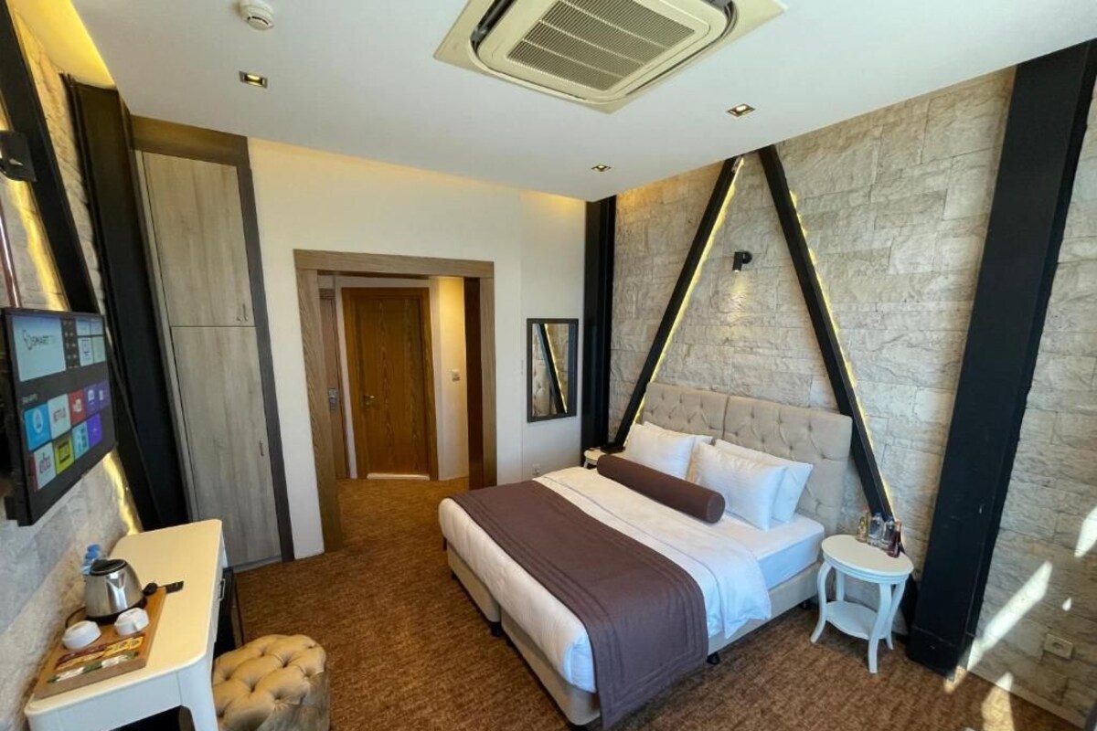 Ein Hotelzimmer mit einem Bett, einem kleinen Tisch, einem Sessel, einem an der Wand befestigten Fernseher und einer Tür.