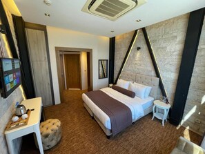 Ein Hotelzimmer mit einem Bett, einem kleinen Tisch, einem Sessel, einem an der Wand befestigten Fernseher und einer Tür.