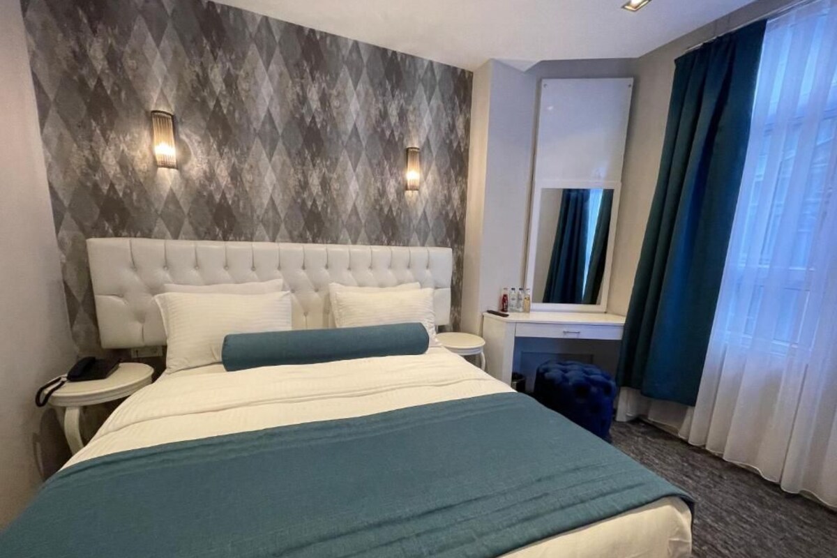 Ein Hotelzimmer mit einem großen Bett, einem Nachttisch, einem Spiegel und einem Fenster mit Vorhängen.