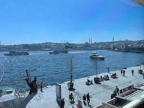 A waterfront promenade with boats, seating areas, and a view of a city skyline. - Weingart Port Seaside Hotel (Istanbul)