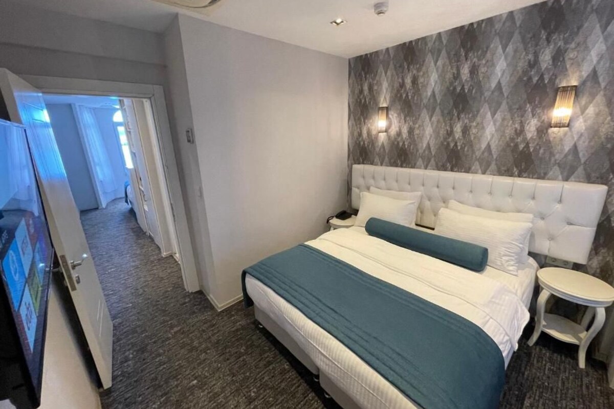 Ein Hotelzimmer mit einem Bett, einem Nachttisch, einem Fernseher und einer Tür zu einem weiteren Raum.