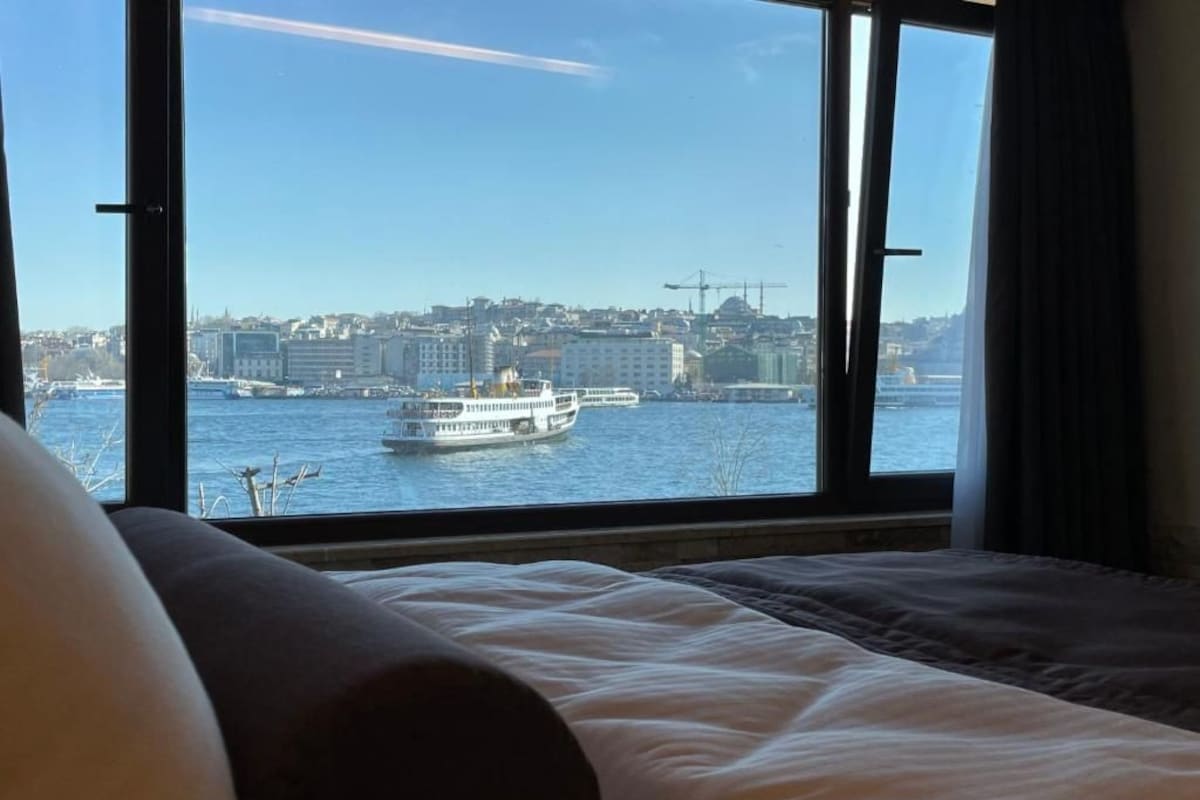 A hotel room with a large window offering a view of a cityscape and a ferry.