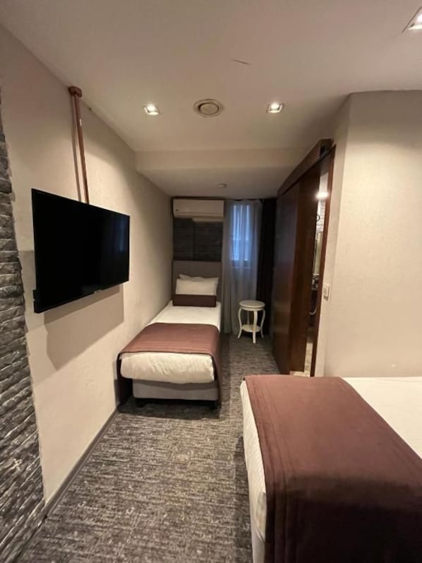 A hotel room with a bed, a TV mounted on the wall, a small table, and a shower area. - Weingart Port Seaside Hotel (Istanbul)