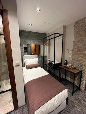 A hotel room with a bed, a bedside table, a wardrobe, and a stone accent wall. - Weingart Port Seaside Hotel (Istanbul)