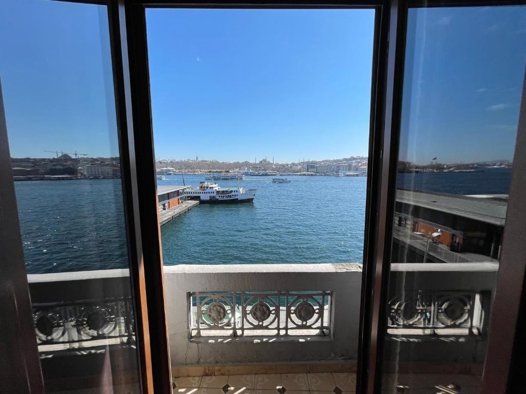 Blick vom Balkon mit Geländer auf ein Gewässer mit Booten und eine entfernte Stadtlandschaft.