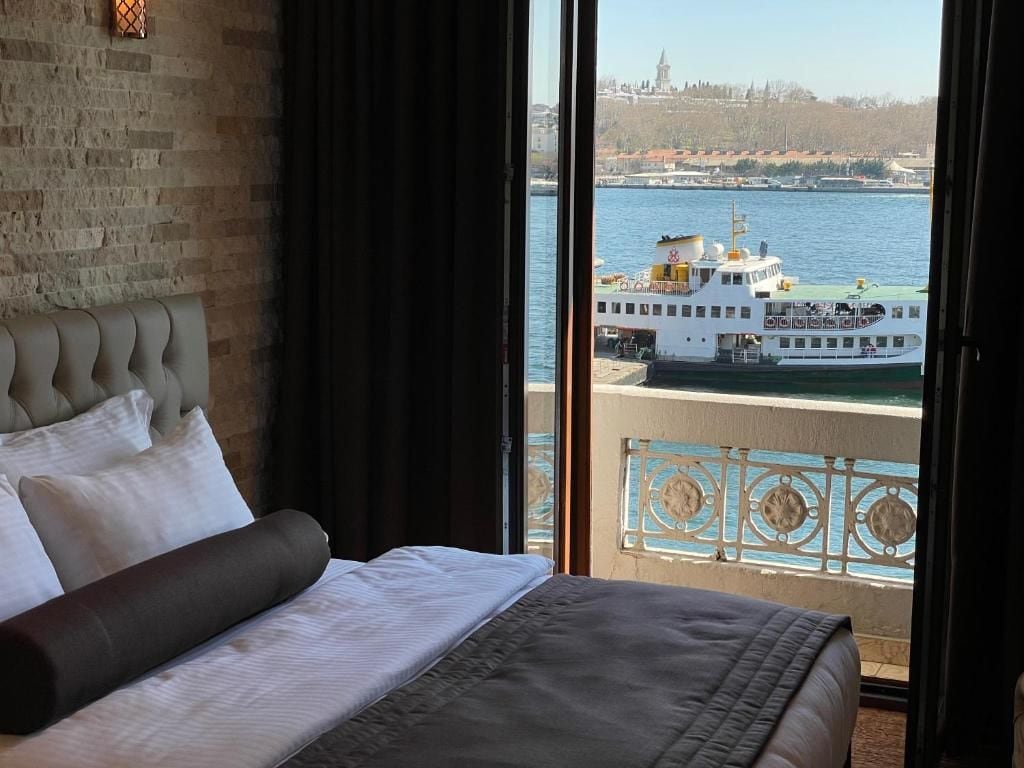 Una habitación de hotel con una cama, vistas a un río y un balcón con barandilla.