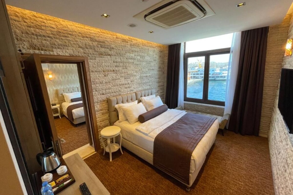 Ein Hotelzimmer mit einem großen Bett, einem kleinen Nachttisch, einem Spiegel und Blick auf das Wasser.