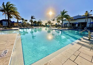 A clear swimming pool with a tiled deck, surrounded by palm trees and umbrellas, under a sunny sky. - Beautiful Villa at Championsgate (Four Corners)