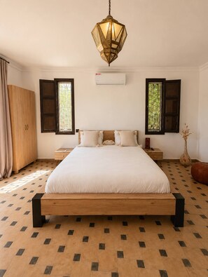 Ein Schlafzimmer mit einem großen Bett, zwei Fenstern mit Rollläden, einer Klimaanlage und einer Hängeleuchte.