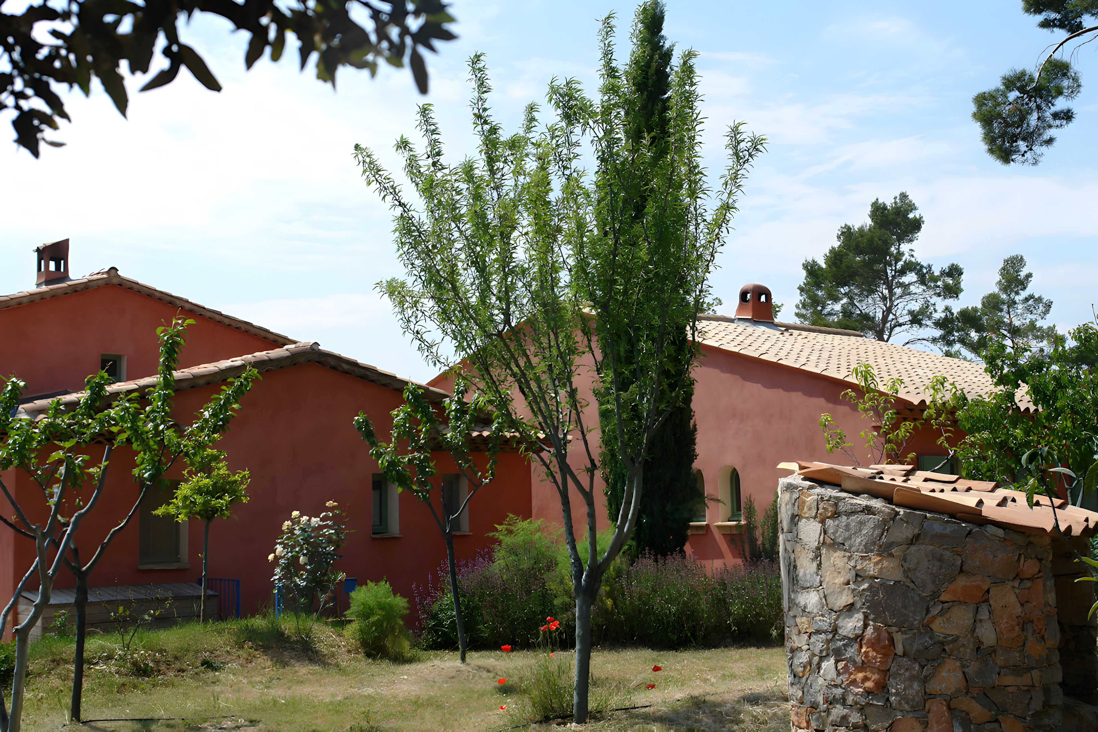 A red building with a tiled roof, surrounded by greenery and a stone wall.