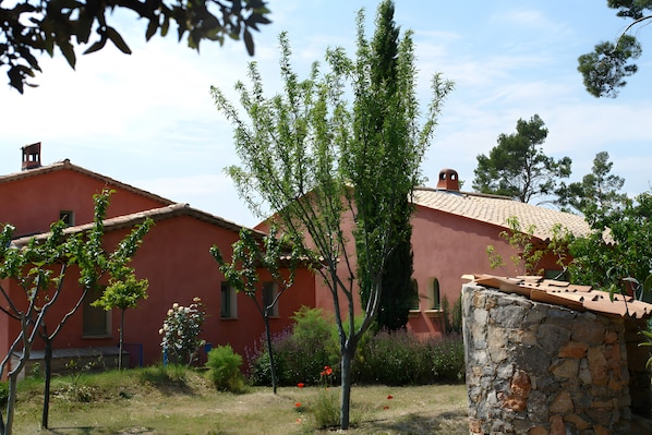 A red building with a tiled roof, surrounded by greenery and a stone wall.