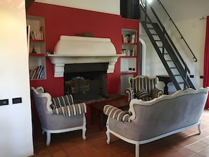 A living room with a fireplace, two armchairs, a bookshelf, and a staircase.