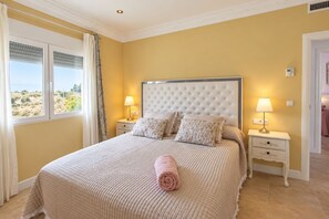 Un dormitorio con una cama grande, dos mesitas de noche con lámparas, una ventana con cortinas y vistas al exterior.