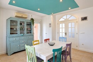 Un comedor con una mesa blanca, sillas de colores, un armario azul con puertas de cristal y una puerta blanca con paneles de vidrio.