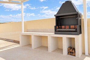 An outdoor barbecue area with a grill, seating, and a view of the sky.