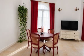 A dining area with a round table, four chairs, a television on a stand, and a plant against the wall.