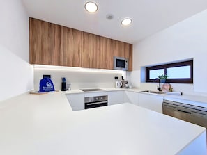 Une cuisine moderne avec des plans de travail blancs, des armoires en bois, un four à micro-ondes encastré, une machine à café et un lave-vaisselle.