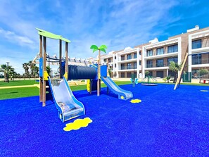 Ein Spielplatz mit Rutschen und Klettergerüsten, umgeben von einem Gebäude mit zahlreichen Fenstern und Balkonen.