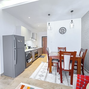 Una cocina compacta con electrodomésticos modernos, un comedor con mobiliario de madera y una alfombra estampada.