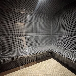 A room with a tiled floor and walls, a bench, and a drain in the corner. - Kilimani Nairobi Luxury Stay | Pool, Gym, Sauna | 1 bedroom (Nairobi)