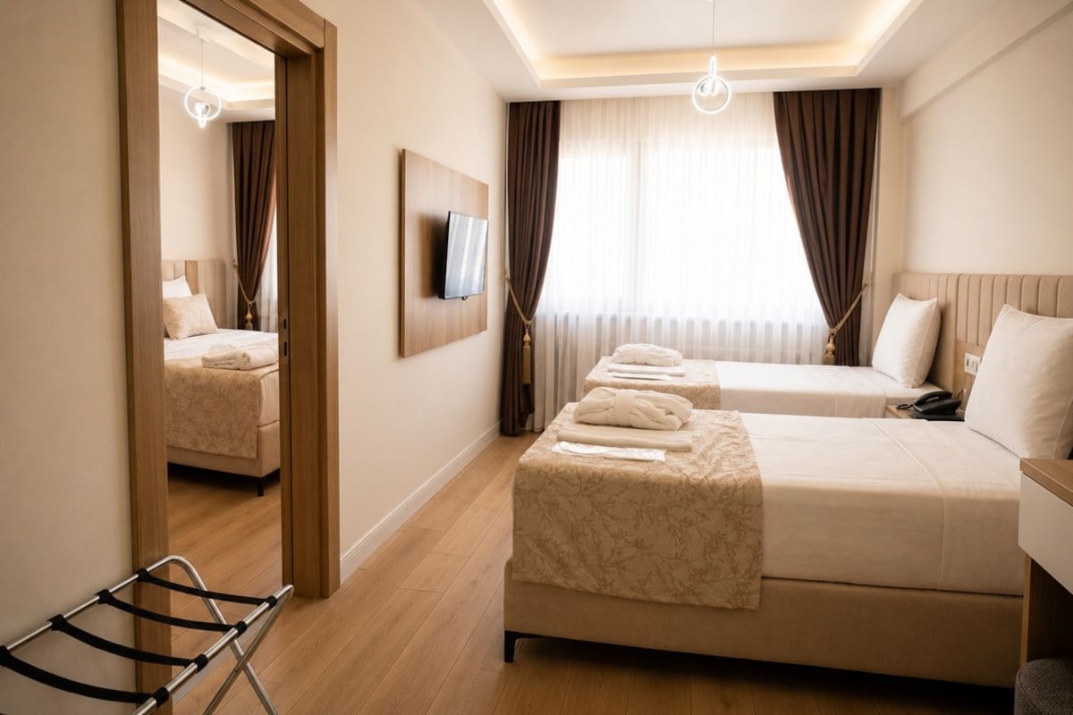 Habitación de hotel con una cama grande, una cama más pequeña, un televisor montado en la pared y un espejo que refleja la habitación.