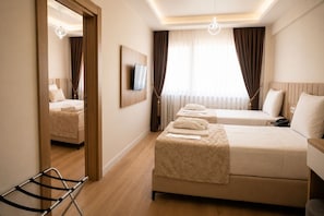 Habitación de hotel con una cama grande, una cama más pequeña, un televisor montado en la pared y un espejo que refleja la habitación.