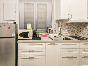 A kitchen with a microwave, kettle, and kettle stand. There are cabinets and a window with blinds. - Al Nido - Studio Apartment in Turin (Torino)