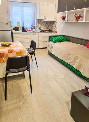 A compact bedroom with a bed, a desk with a chair, a kitchenette, and a window. - Al Nido - Studio Apartment in Turin (Torino)