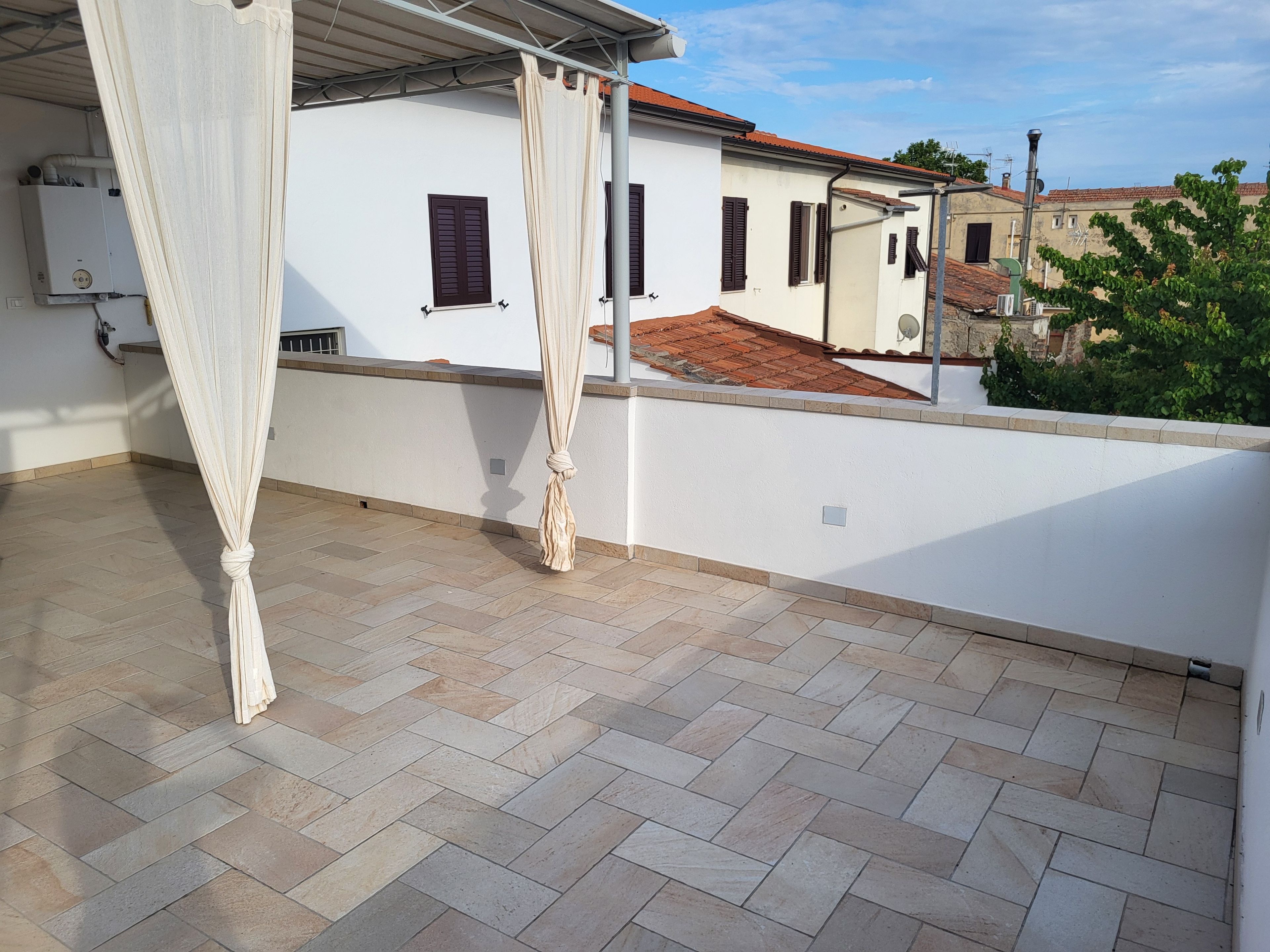 Una terraza en la azotea con pared blanca, suelo de baldosas y cortina blanca.
