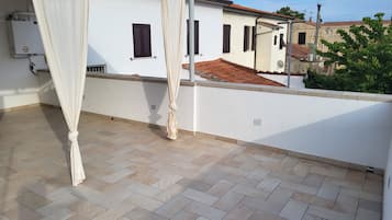 Una terraza en la azotea con pared blanca, suelo de baldosas y cortina blanca.