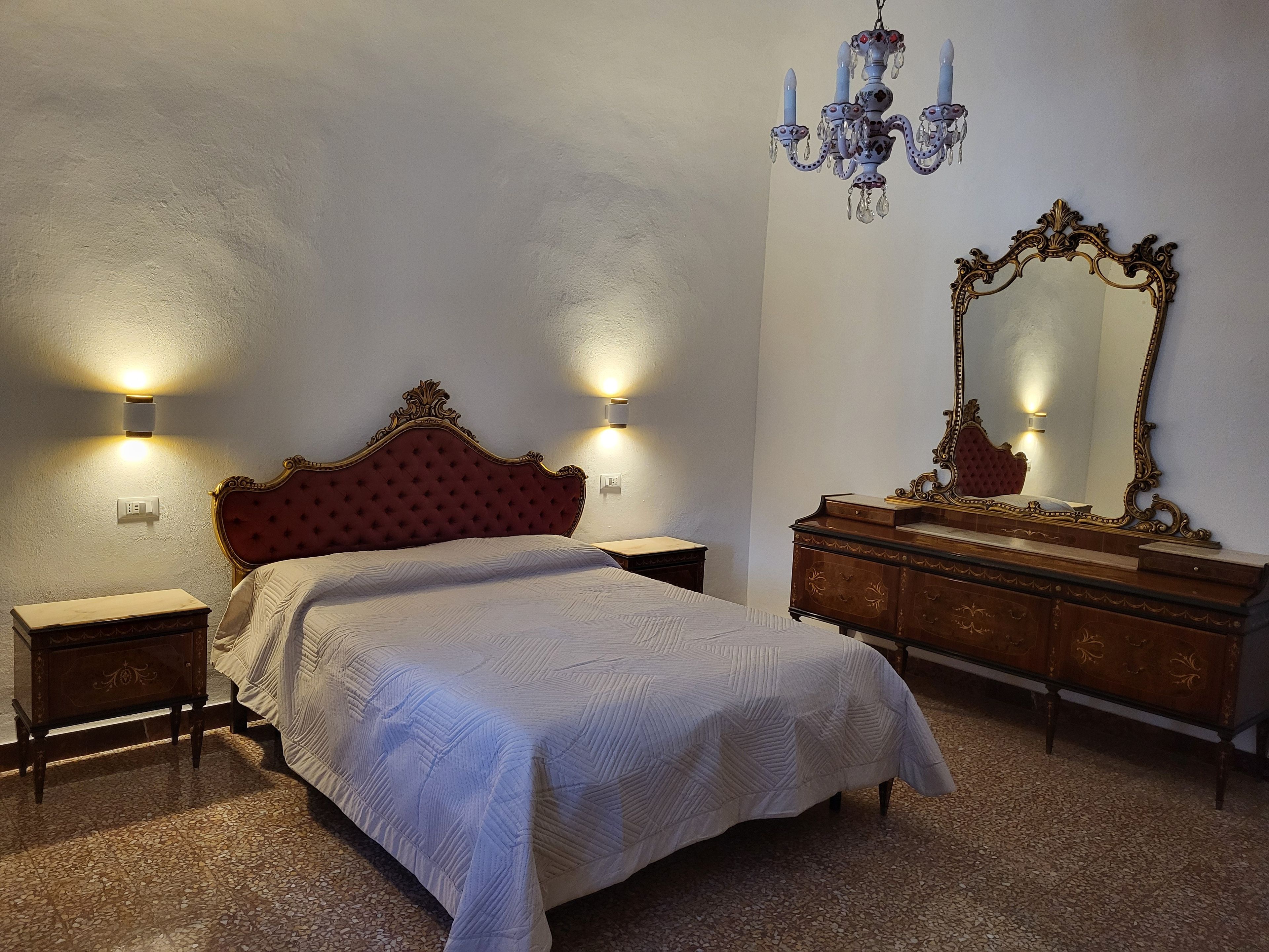 Ein Schlafzimmer mit einem Bett, Nachttischen, einer Kommode, einem Spiegel und einer Kronleuchter.