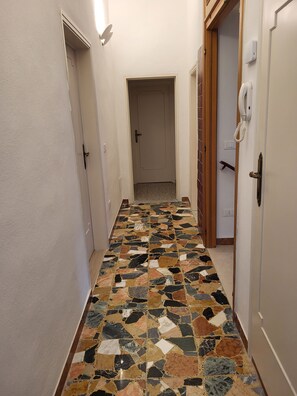 Un passadís amb terra de rajola estampada, portes a banda i banda i un interruptor a la paret.