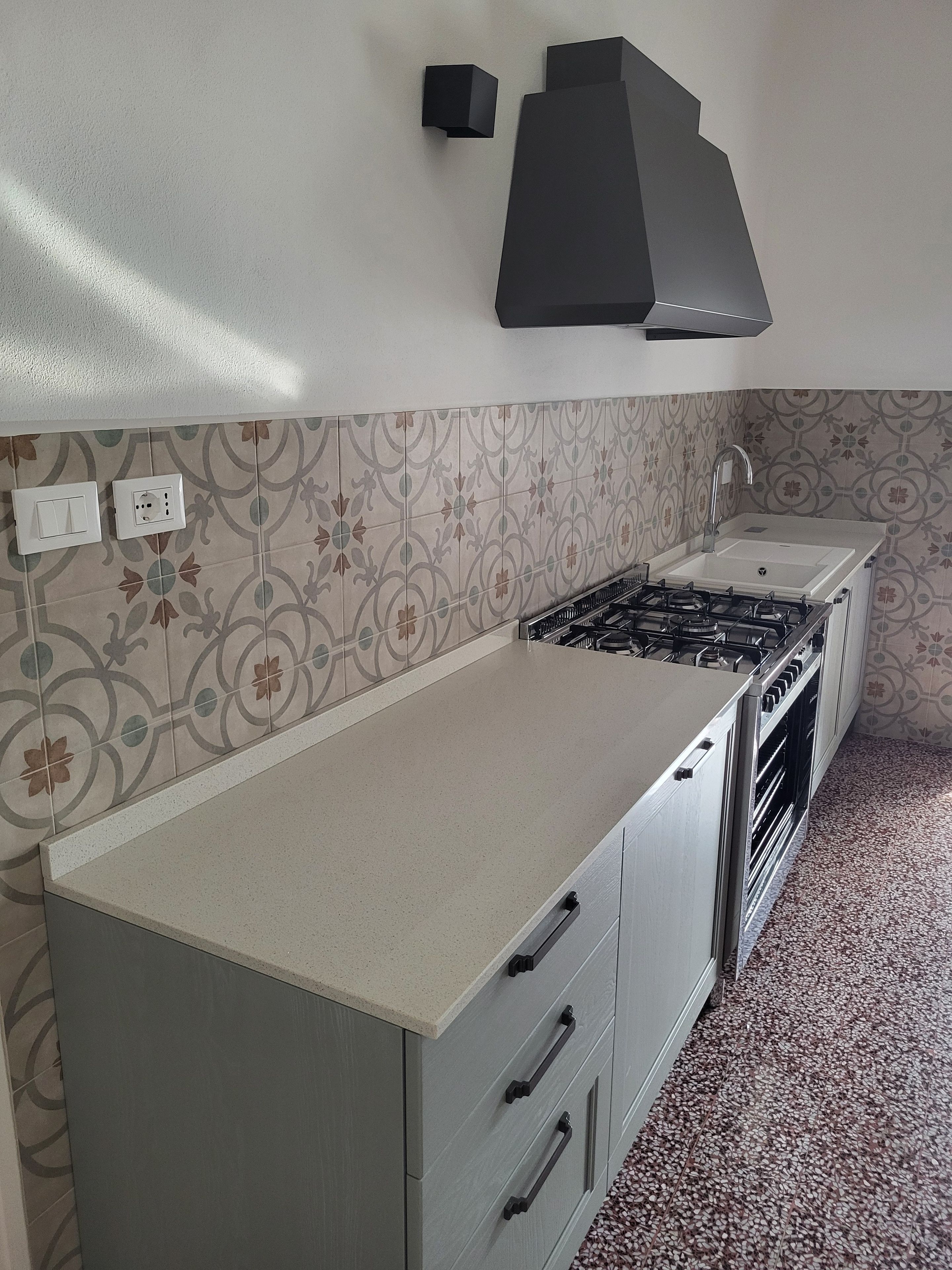 Una cocina con estufa a gas, un fregadero y azulejos decorados.