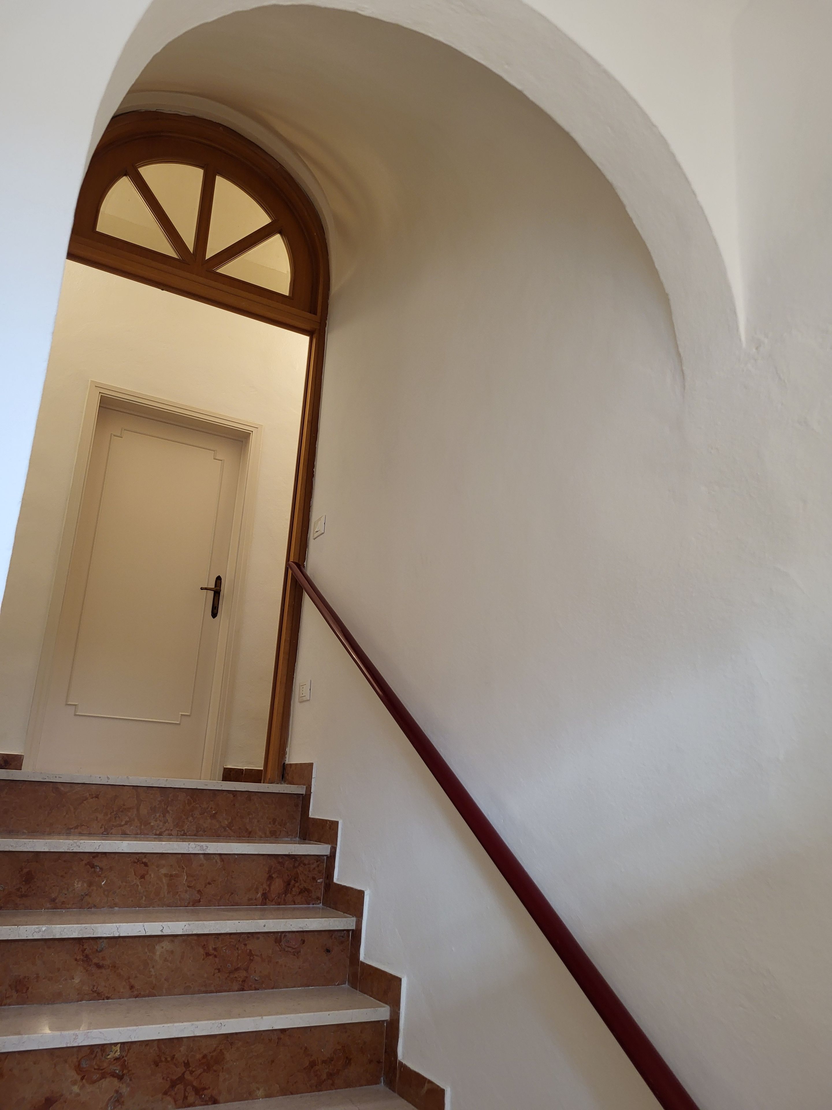Una escalera con barandal de madera y una puerta blanca al final.