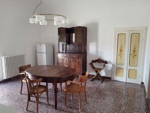 A dining area with a round wooden table, four chairs, a white refrigerator, a wooden cabinet, and a door with floral decorations.